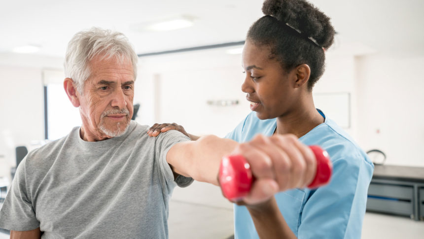 Man holding small dumbbell receiving physical therapy from therapist