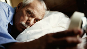 Image of man in bed with head on pillow, looking at alarm clock