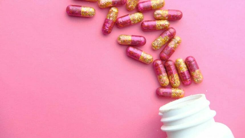 Image of multivitamins scattering from opening bottle on pink background.