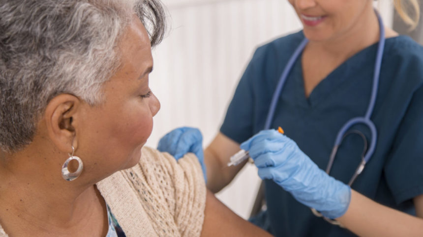 A healthcare provider wearing gloves vaccinates an older woman