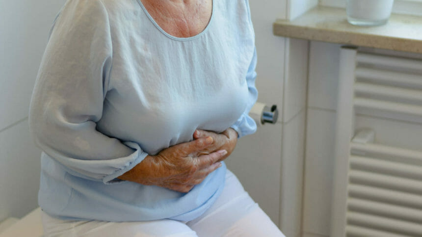 Lower body image of woman with stomach pain, holding stomach in bathroom