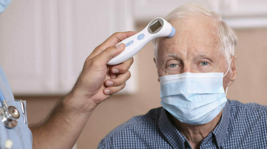 Healthcare worker checks fever of patient with infrared thermometer. Both wear protective face masks.