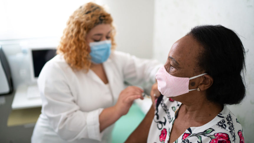 Nurse applying vaccine on patient's arm wearing face mask