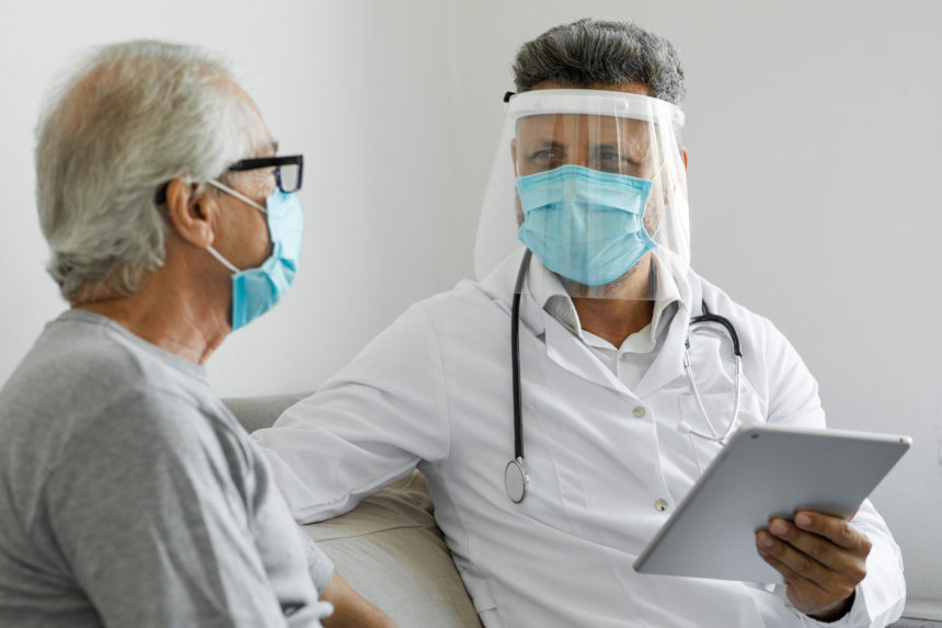 Image of a senior man being visited by a clinician, both wearing face masks