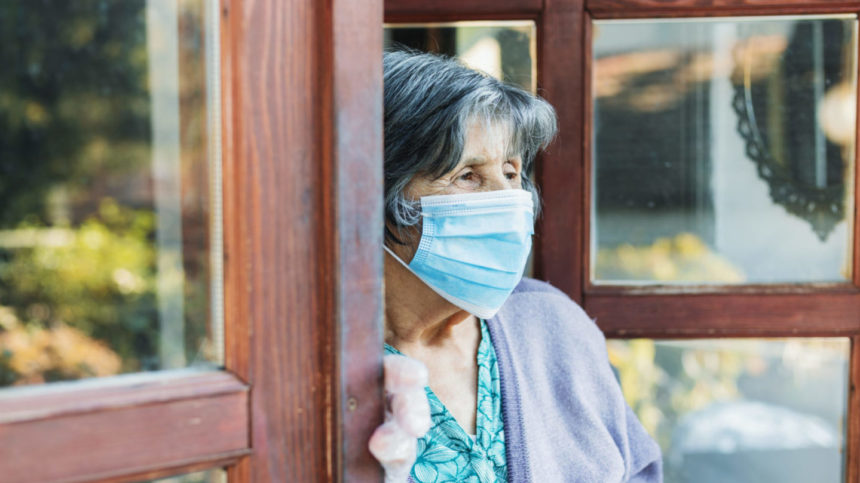 Image of senior woman with a mask looking wistfully out a door