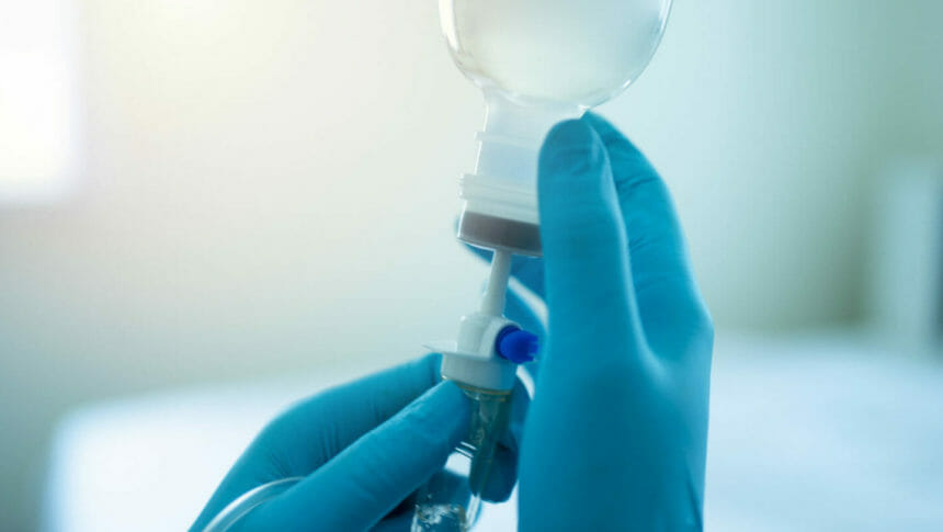 Doctor, clinician wearing surgical gloves, readying an intravenous infusion