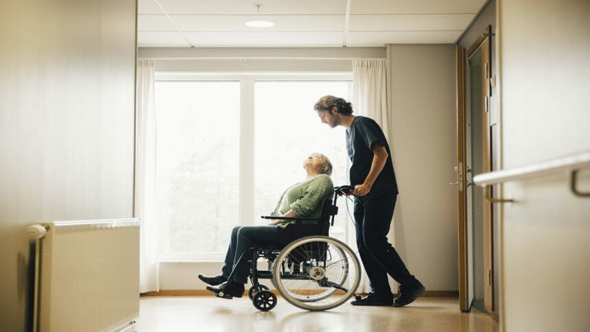 Image of male nurse pushing senior woman in a wheelchair in nursing facility