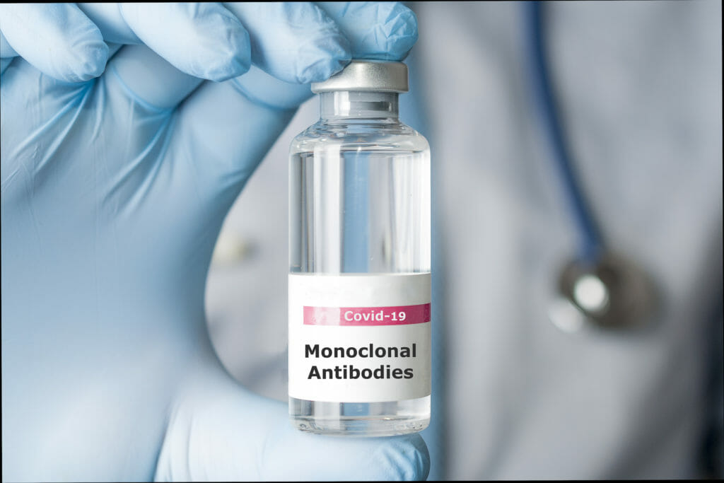 Image of doctor's gloved hand holding a vial of monoclonal antibodies