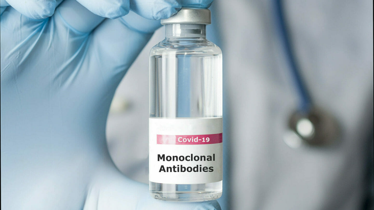 Image of doctor's gloved hand holding a vial of monoclonal antibodies