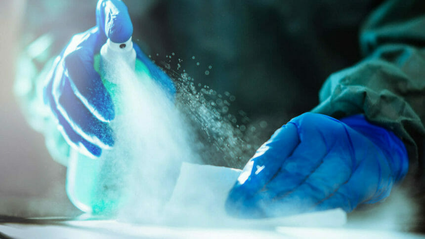Closeup image of gloved hands spraying surface with disinfectant for infection control