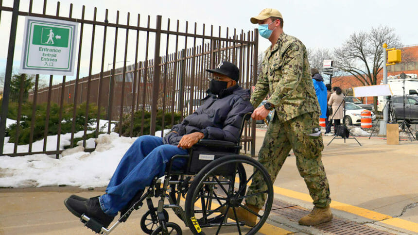 National Guard member helps a person in a wheelchair enter a facility
