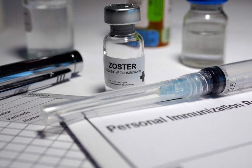 Image of a vial of shingles vaccine labeled "zoster vaccine (recombinant)" on a clinician's work desk.