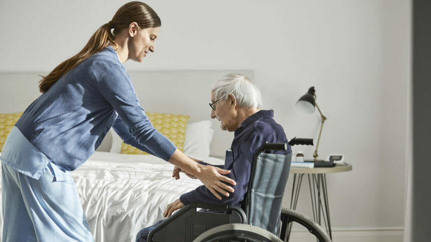 Nurse supporting senior man to sit on wheelchair