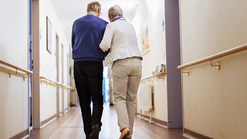 Woman assisting older man to walk in assisted living facility hallway