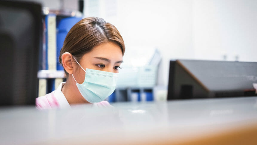 A masked nurse works at a computer
