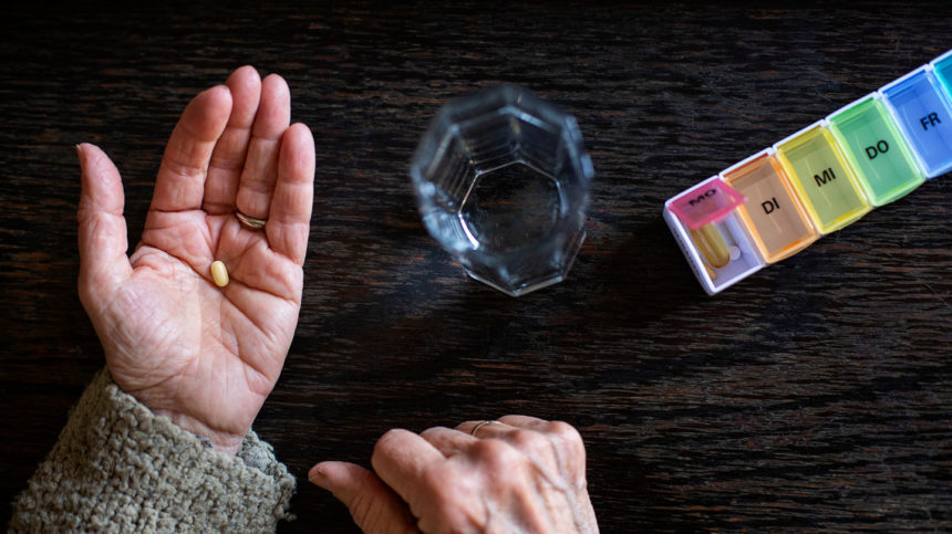 Closeup of open hand holding pill next to glass of water and pill box