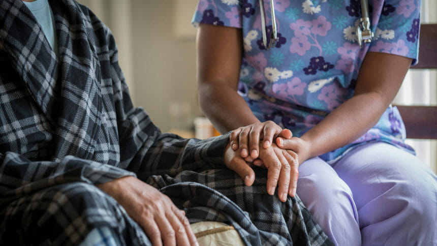 A nurse holds hands with a senior nursing home resident