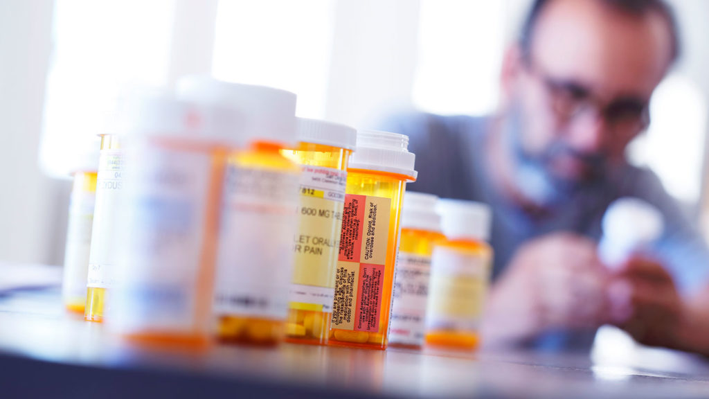 A senior man is surrounded by medicine prescription bottles