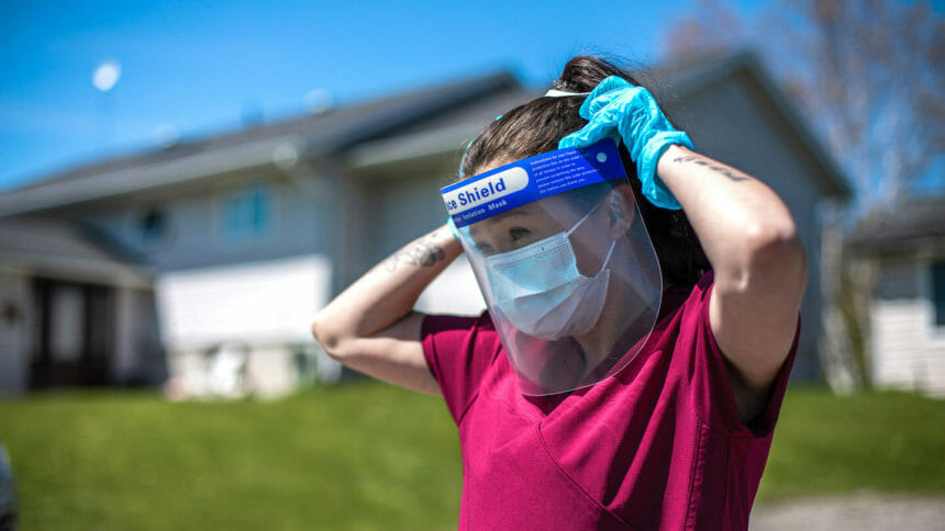 A nurse puts on protective equipment before performing house call.