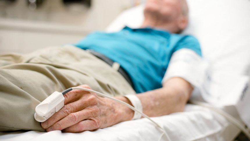 A Senior man is lying down on a hospital bed while taking pulse oximetry