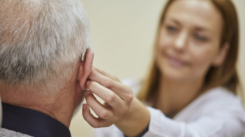 Image of female doctor applying hearing aid to senior man's ear