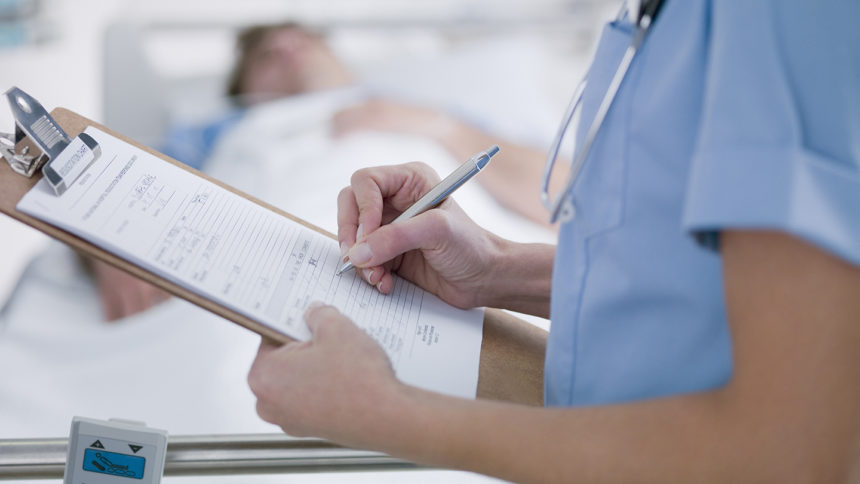 Closeup of nurse making notes near patient's bed