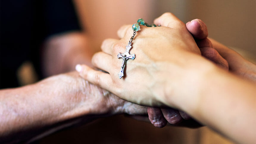 Cropped shot of a senior woman being comforted by her nurse while holding a rosary
