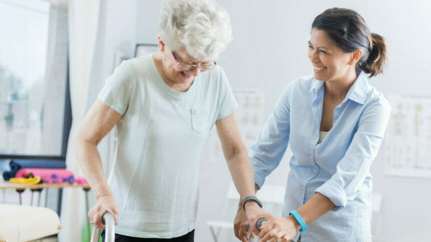Healthcare professional helps senior woman walk with a walker