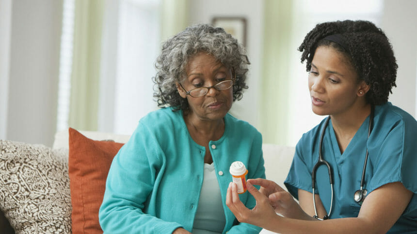 Home nurse reviewing prescription bottle with patient