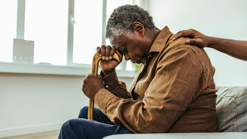 African-American man showing grief while leaning on cane