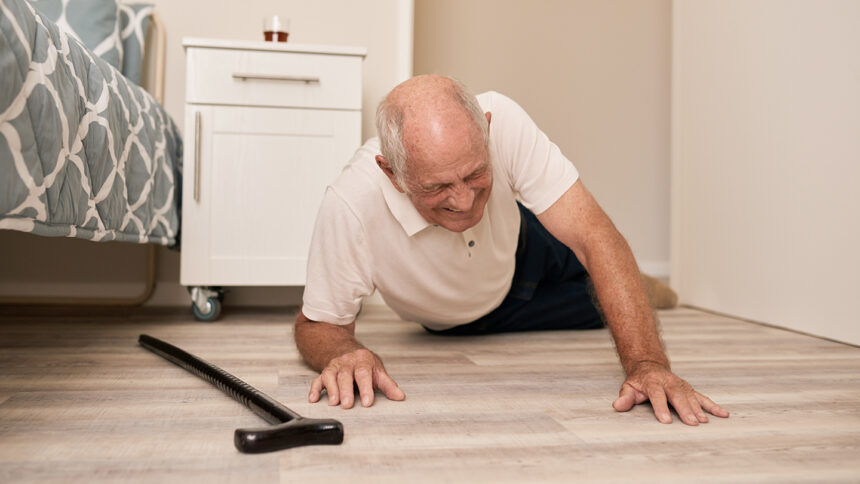 Image of senior man wincing in pain beside his walking cane after falling on the floor of his room in an assisted living home