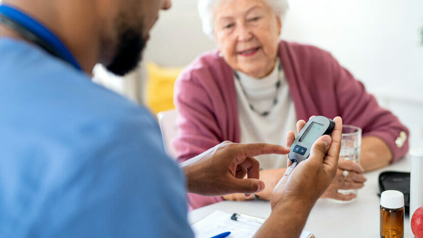 Male nurse or caregiver doing a finger sugar test to senior woman indoors during home visit.