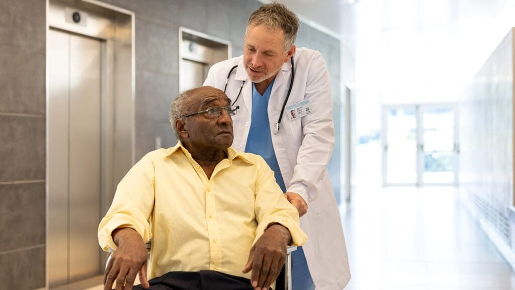 Doctor moving a senior African American patient on a wheelchair at the hospital and talking to him - healthcare and medicine concepts